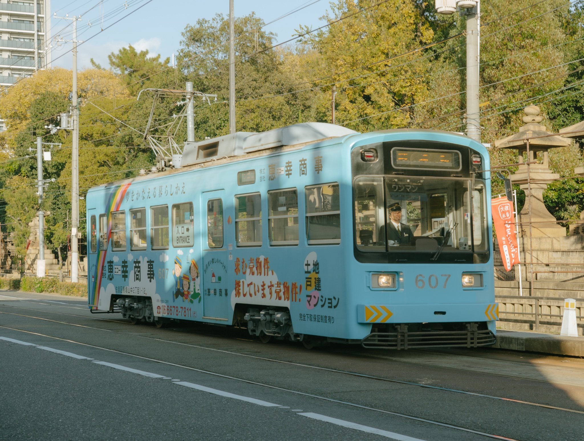 Blue Hankai tram passing stone lanterns in Osaka